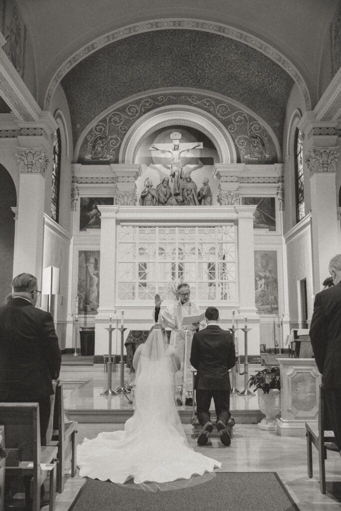 A bride and groom kneel during the nuptial blessing.