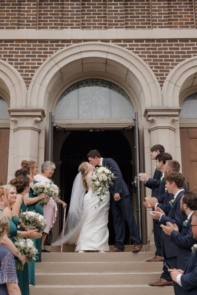 The bride and groom give a kiss while exiting the ceremony.