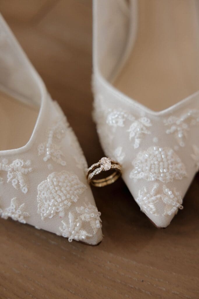 A close up of a wedding band between the bride's shoes.